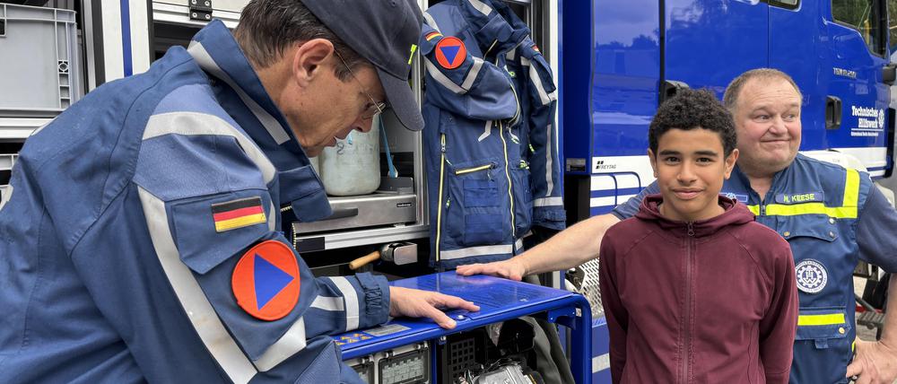 Ein Schüler steht vor einem Einsatzwagen des Technischen Hilfswerks (THW) gemeinsam mit zwei THWlern, die ihm die Ausrüstung zeigen.