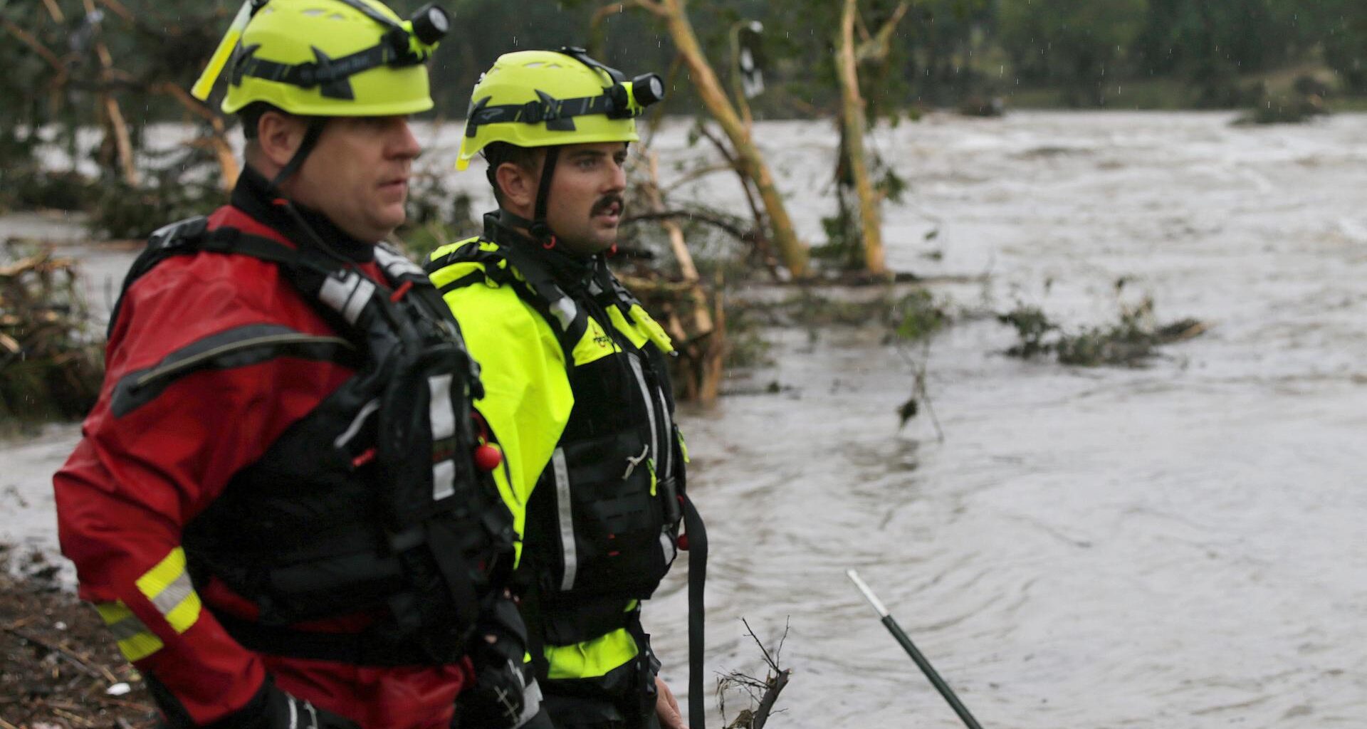 Feuerwehrmänner stehen an einem Flussufer und blicken auf reißende Fluten.