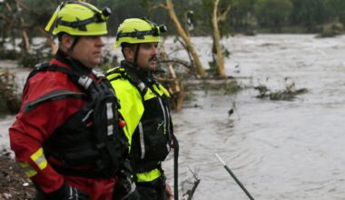 Feuerwehrmänner stehen an einem Flussufer und blicken auf reißende Fluten.