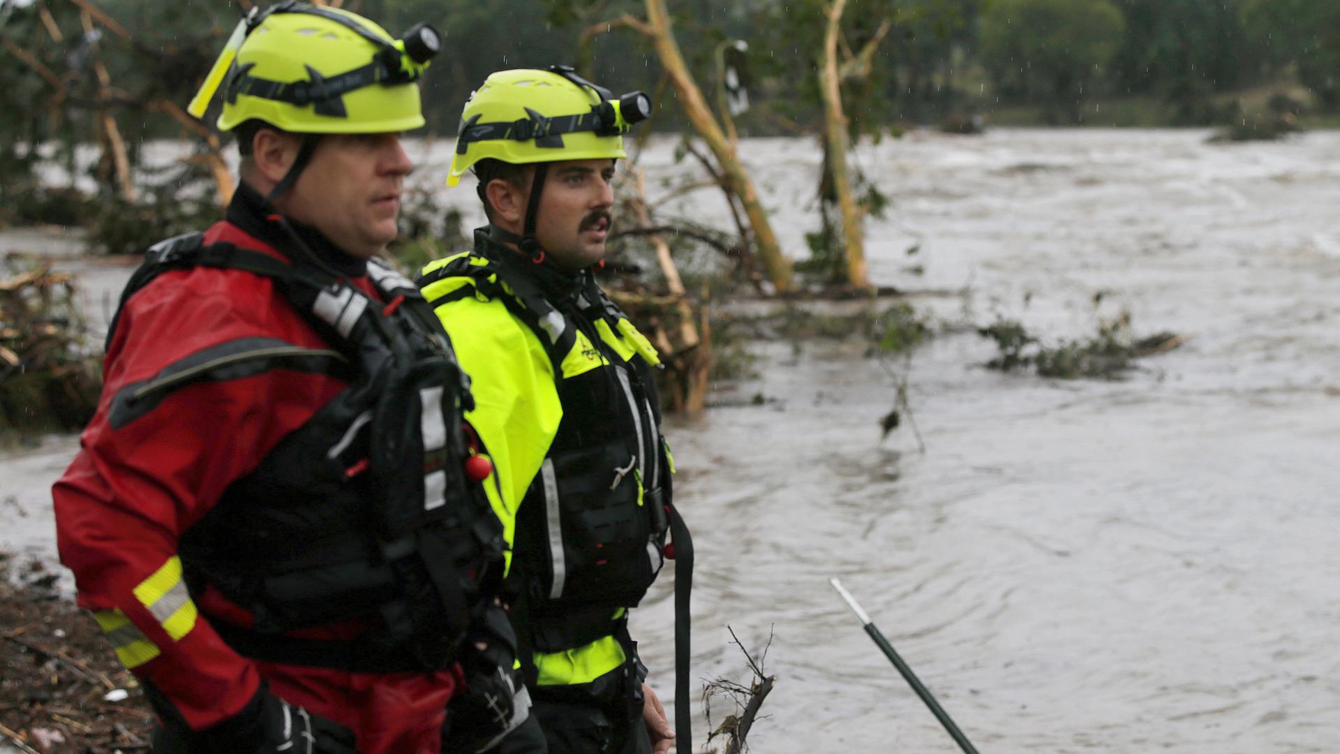 Feuerwehrmänner stehen an einem Flussufer und blicken auf reißende Fluten.