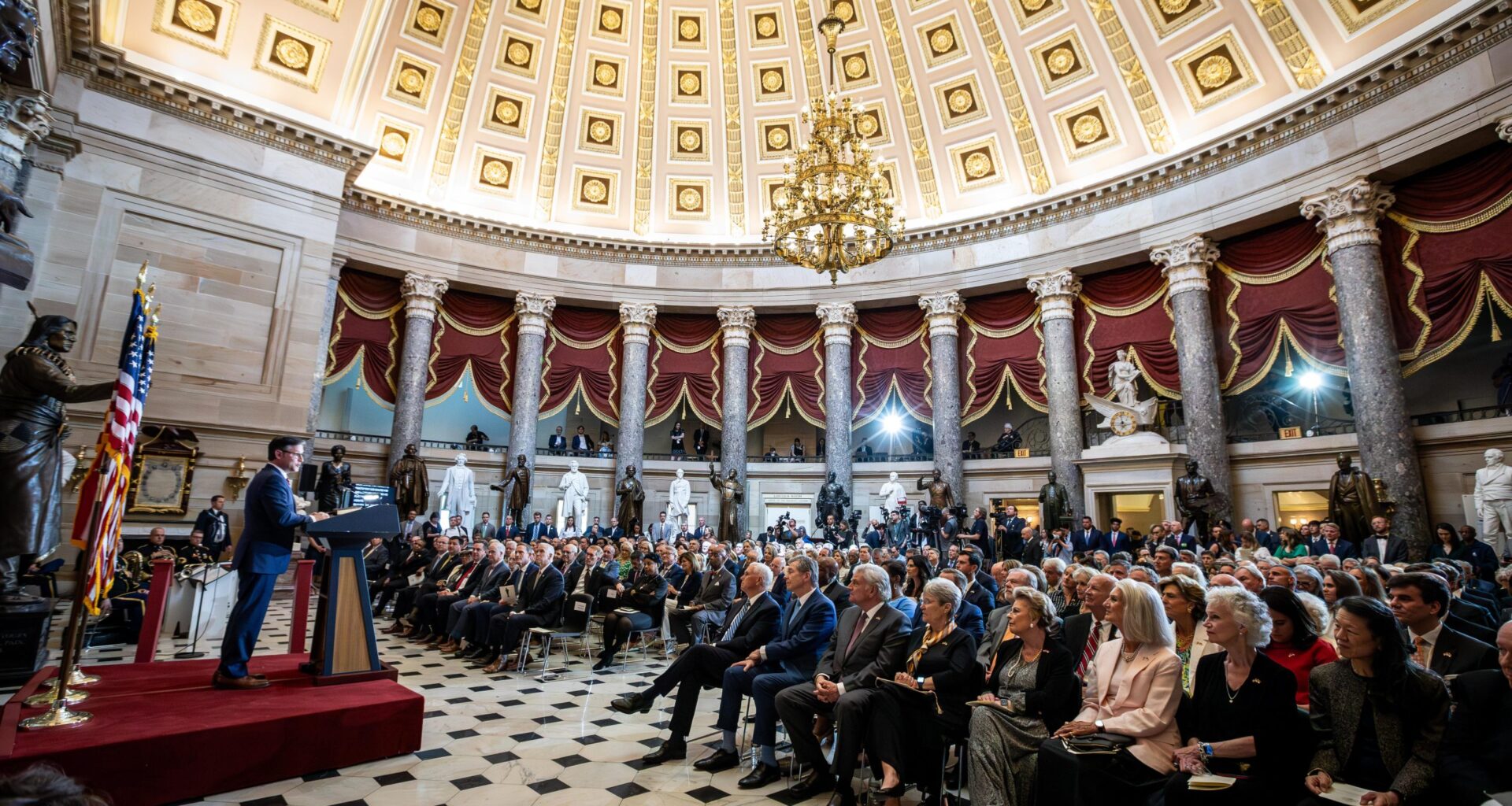 Ein Redner spricht vor einem sitzenden Publikum in einem großen Saal mit Kuppel, Kronleuchtern, Statuen und amerikanischen Flaggen über die Krypto-Gesetze vor dem US-Kongress.