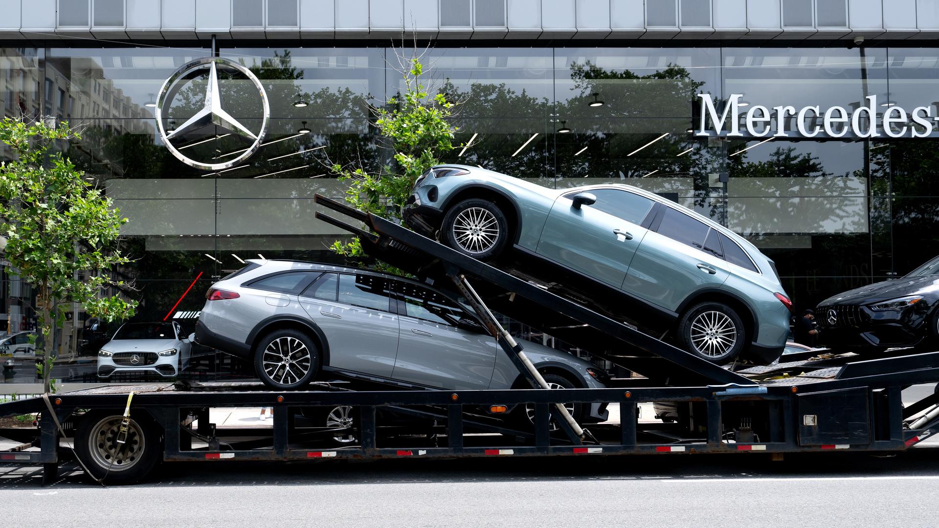Ein Autotransporter mit Neuwagen von Mercedes-Benz steht vor einem Autohaus.
