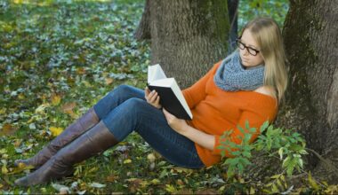 Junge Frau mit Brille sitzt im Park und liest ein Buch.