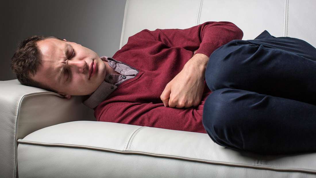 Ein Mann liegt krank auf dem Sofa.