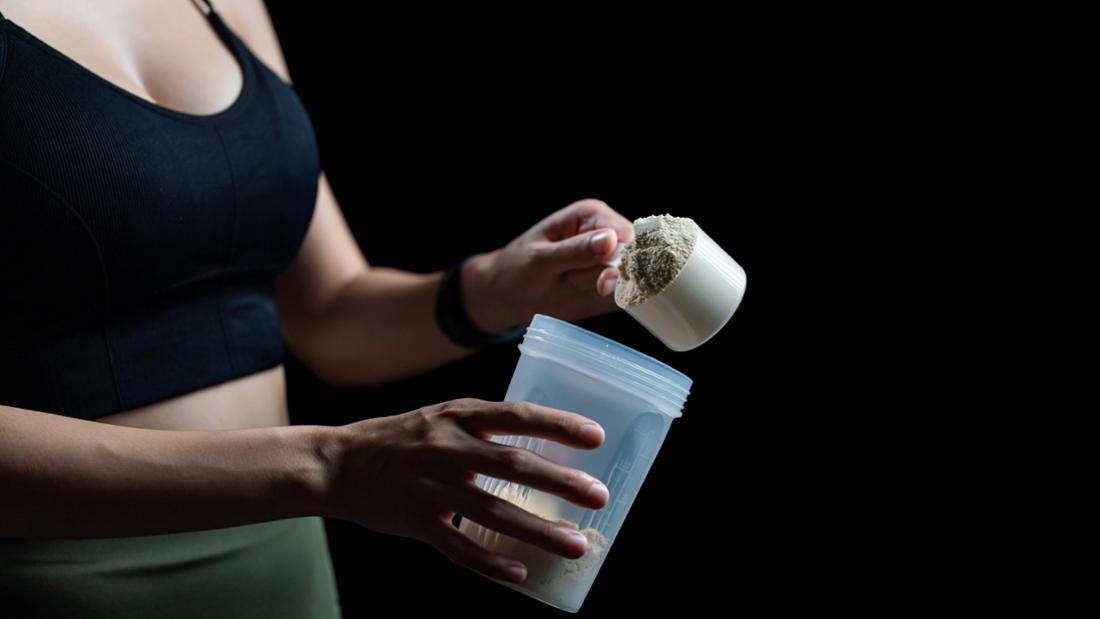 Frau im Sport-Outfit macht sich einen Shake