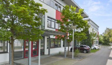 Außenansicht eines modernen Bürogebäudes mit großen Fenstern und umgeben von Bäumen.