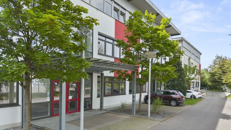 Außenansicht eines modernen Bürogebäudes mit großen Fenstern und umgeben von Bäumen.