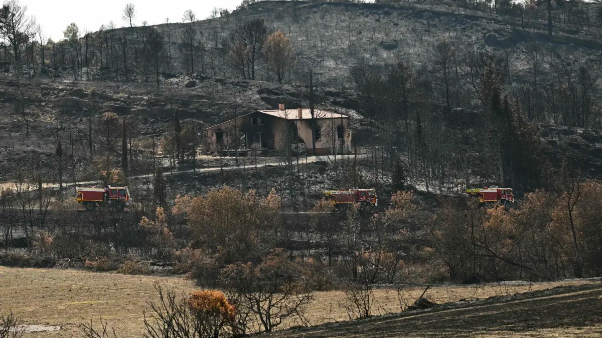 Brand in Südfrankreich: 10.08.2025, Frankreich, Jonquières: Feuerwehrfahrzeuge fahren in Jonquières in Südfrankreich an verbrannter Vegetation und einem ausgebrannten Haus vorbei. Ein großer Flächenbrand in Südfrankreich hält die Feuerwehr noch immer in Atem. Foto: Bertrand Guay/AFP/dpa +++ dpa-Bildfunk +++