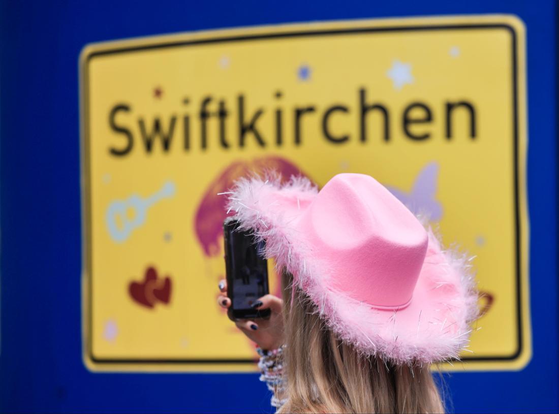 Ein Fan fotografiert vor dem ersten Deutschland-Konzert der Sängerin Taylor Swift in der Gelsenkirchener Innenstadt ein Schild mit der Aufschrift „Swiftkirchen“. 