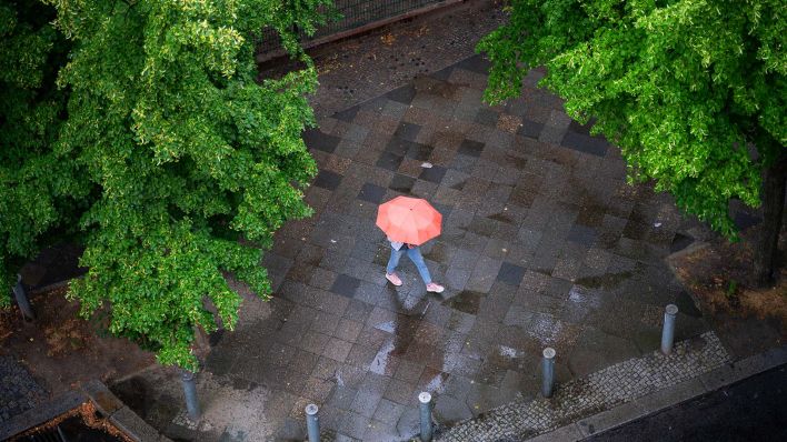 Symbolbild:Eine Person mit Regenschirm geht bei leichtem Regen auf einem nassem Gehweg im Bezirk Charlottenburg-Wilmersdorf entlang.(Quelle:picture alliance/SZ Photo/O.Schülke)