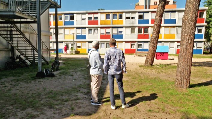 Peter Hermanns und und Baara Mshinish stehen vor einem Gebäude des Containerdorfs im Allende-Viertel und schauen es an.(Quelle:rbb)