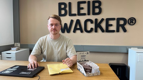 Gründer Matteo Wacker sitzt an seinem Schreibtisch. Im Hintergrund an der Wand steht "bleib wacker" geschrieben.