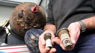 EIn Mitarbeiter des Kampfmittelbeseitigungsdiensts Baden-Württemberg zeigt eine entschärfte Weltkriegsbombe und deren Zünder (Archivbild). 