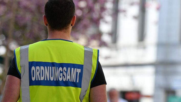 Symbolbild: Ein Mitarbeiter des Ordnungsamtes kontrolliert Menschen auf einem öffentlichen Platz. (Quelle: dpa/Hufnagel)