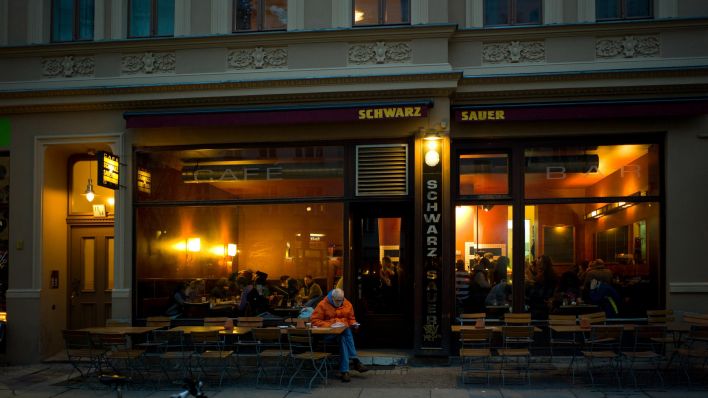 Ein Mann sitzt vor dem geöffneten Café "Schwarz Sauer" im Prenzlauer Berg (Quelle: picture alliance/Caro/Teich).