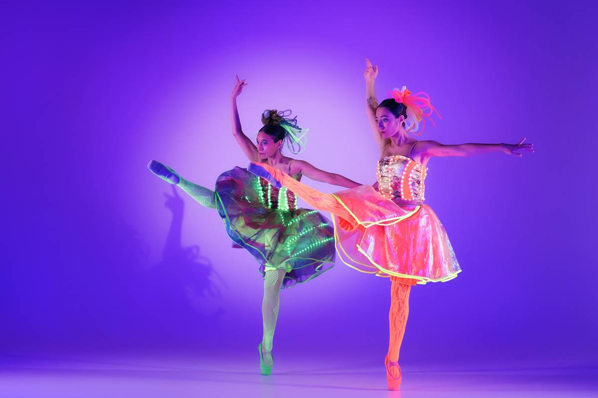 Zwei Ballerinas tanzen nebeneinander mit erhobenen Armen und Beinen bei Ballet of Lights: Cinderella in funkelnden Kostümen.