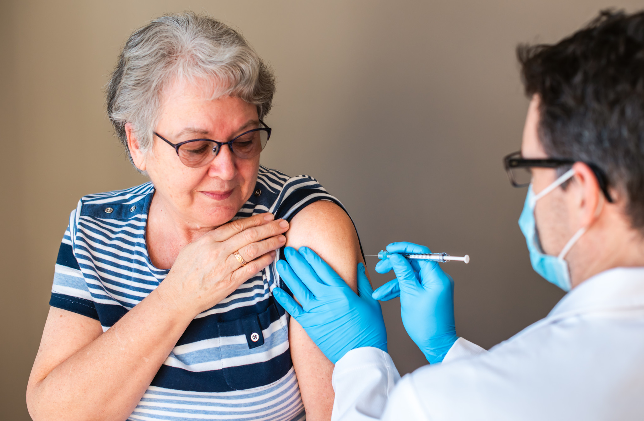 Ältere Frau erhält Impfung in den Arm von einem Arzt, der eine Maske trägt und blaue Laborhandschuhe.
