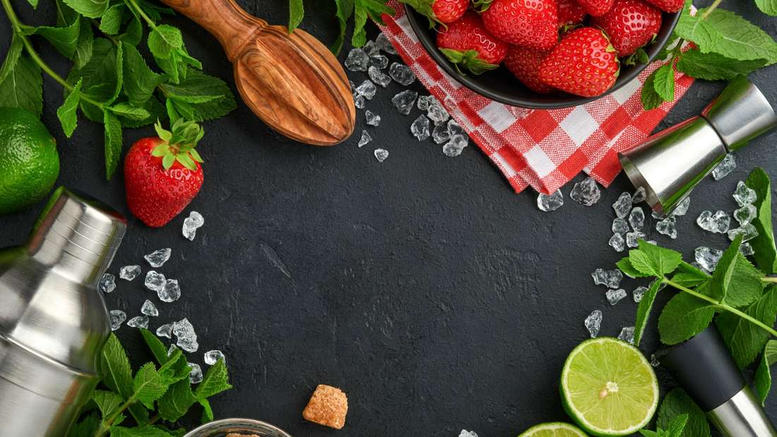 Lebensmittel frische Zutaten für die Herstellung von Limonade, infundiert Detox-Wasser oder Cocktail. Erdbeeren, Limette, Minze, Basilikum, Rohrzucker, Eiswürfel und Shaker auf schwarzem Stein oder Beton Hintergrund
