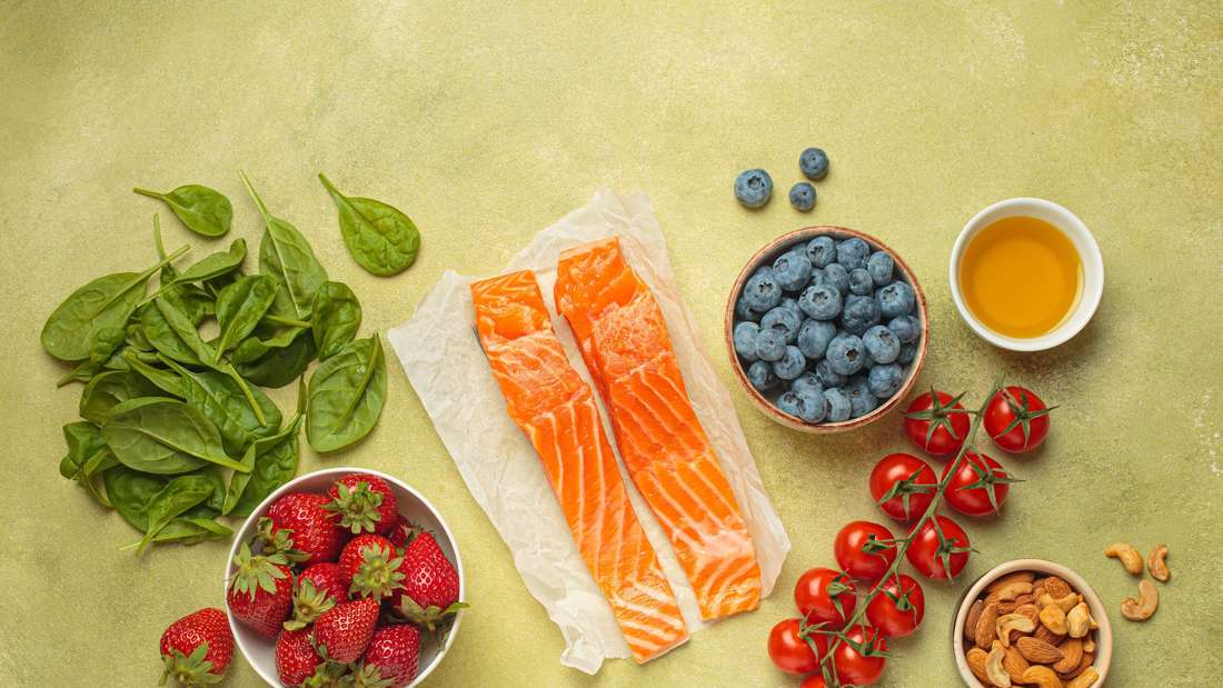 Gesunde Lebensmittel für entzündungshemmende Ernährung: Fisch, Gemüse, Beeren, Nüsse, Olivenöl, Spinat Draufsicht 