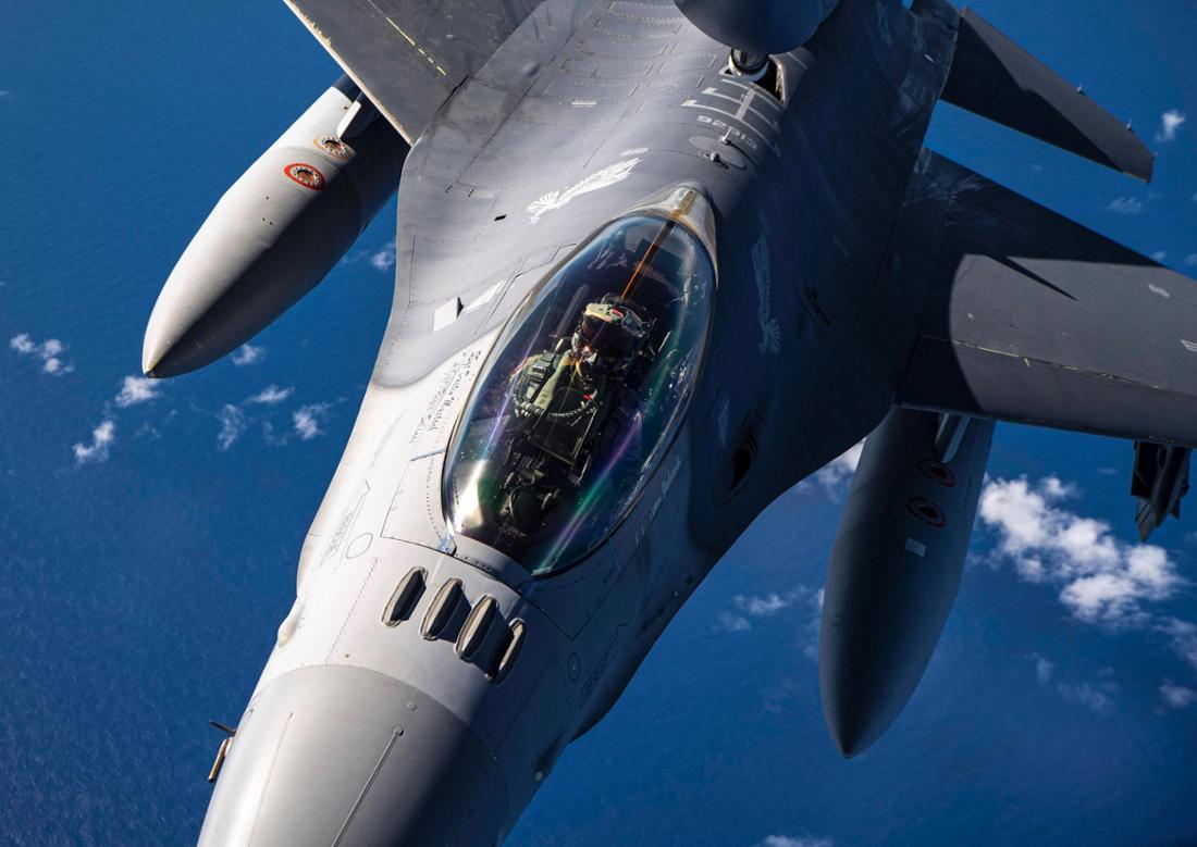 Eine Nahaufnahme des Cockpits einer fliegenden F-16 über blauem Himmel.