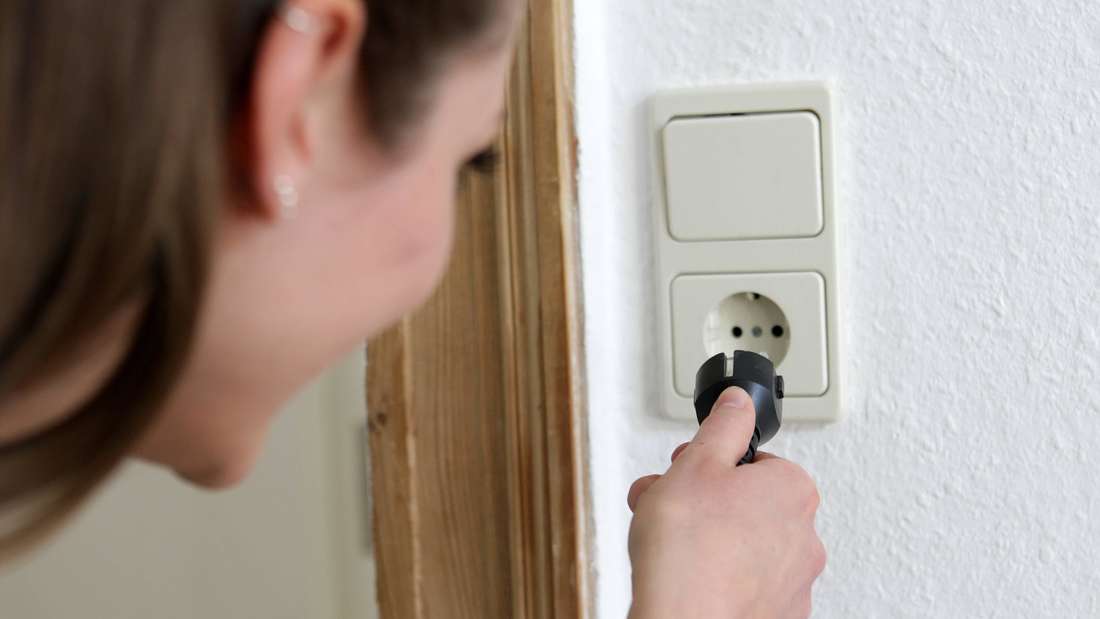 Frau steckt Stecker in eine Steckdose.