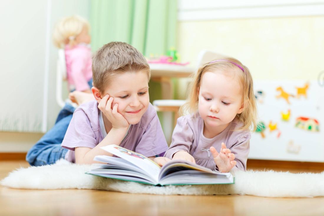 Bruder und Schwester liegen im Kinderzimmer auf dem Boden und lesen zusammen ein Buch (Symbolbild)