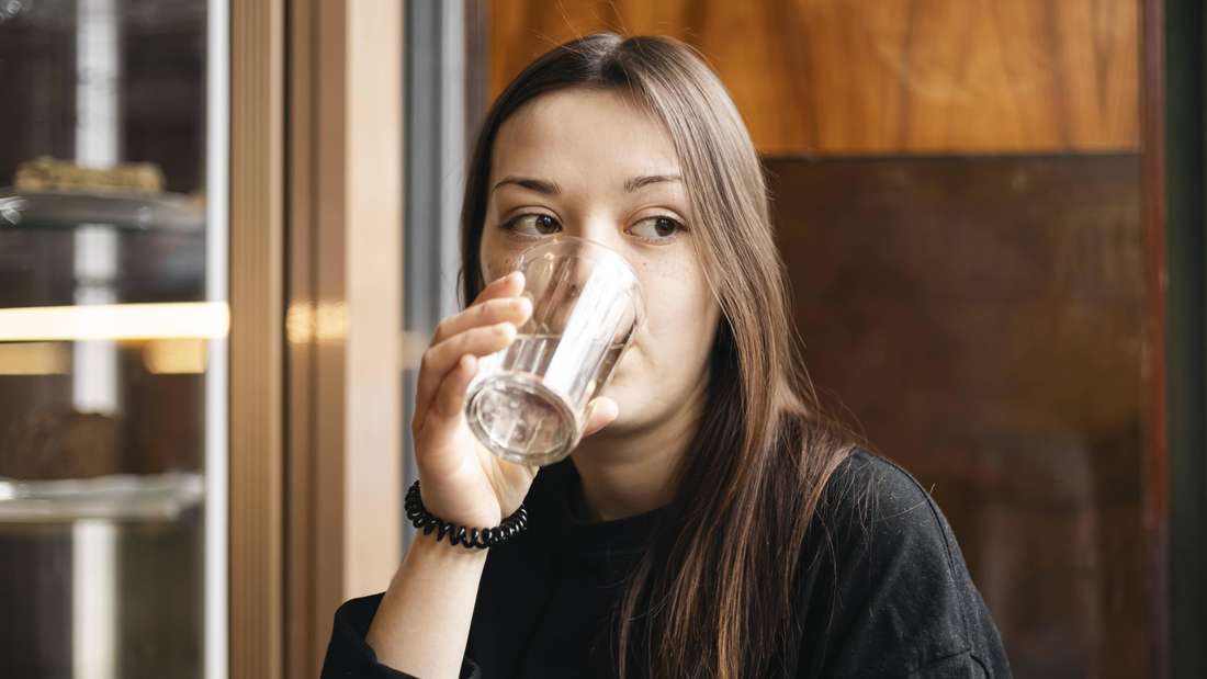 Eine junge Frau trinkt ein Glas Wasser.