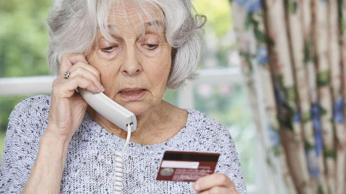 Ältere Frau mit Telefonhörer am Ohr und Bankkarte in der Hand.