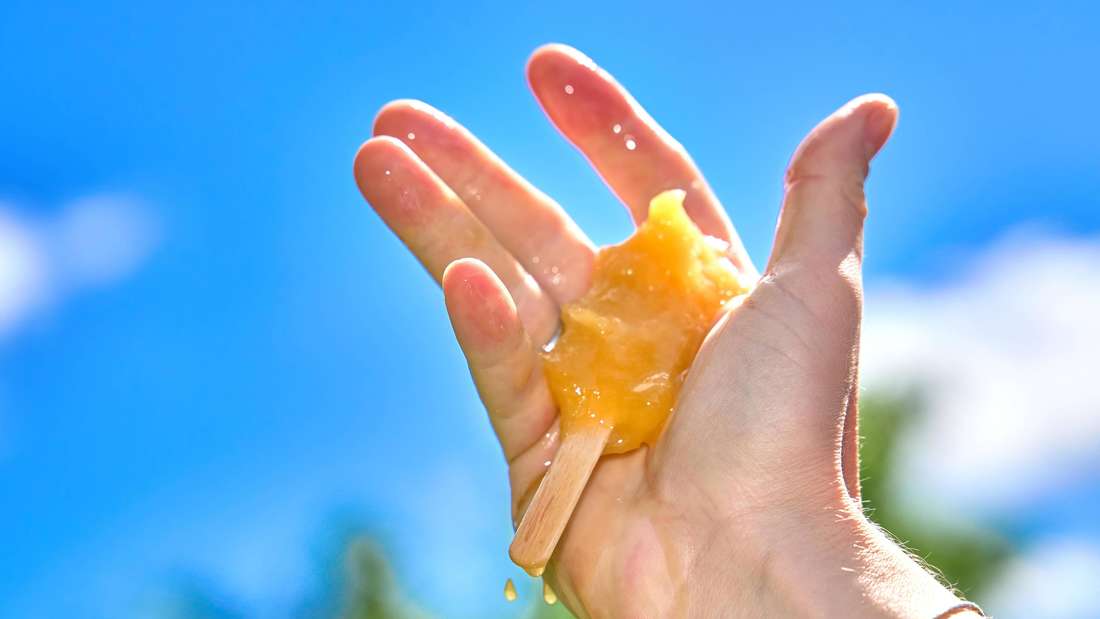 Ein schmelzendes Eis am Stiel in der Hand.