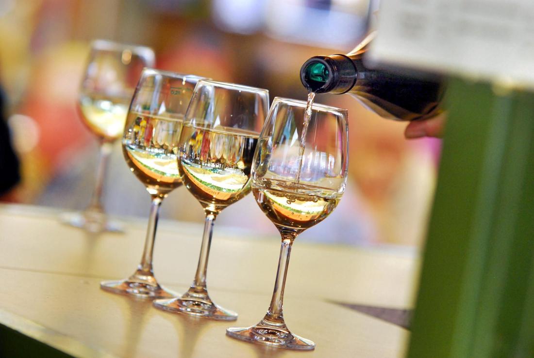 Drei Weingläser stehen auf einer Theke. Zwei Gläser sind bereits befüllt, in ein drittes Glas wird gerade Wein eingegossen. 