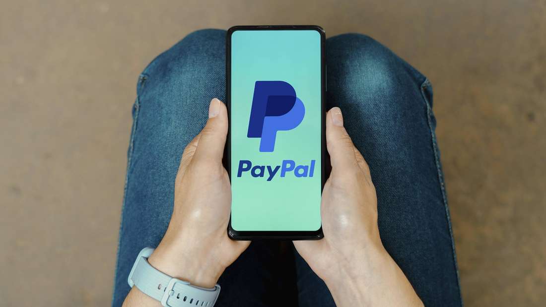 Person mit Smartphone in den Händen. Auf dem Display ist das PayPal-Logo zu sehen.