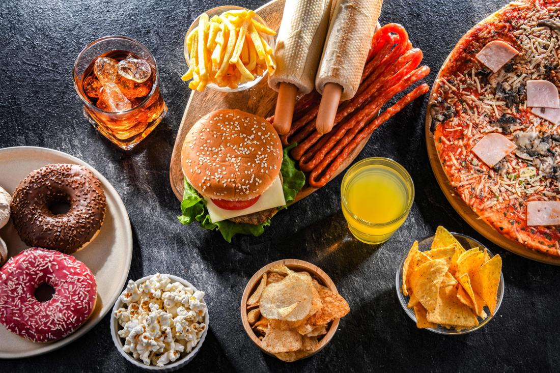 Eine Auswahl an Junkfood auf einem Tisch serviert, darunter Burger, Pommes, Pizza, Donuts und weiteres.