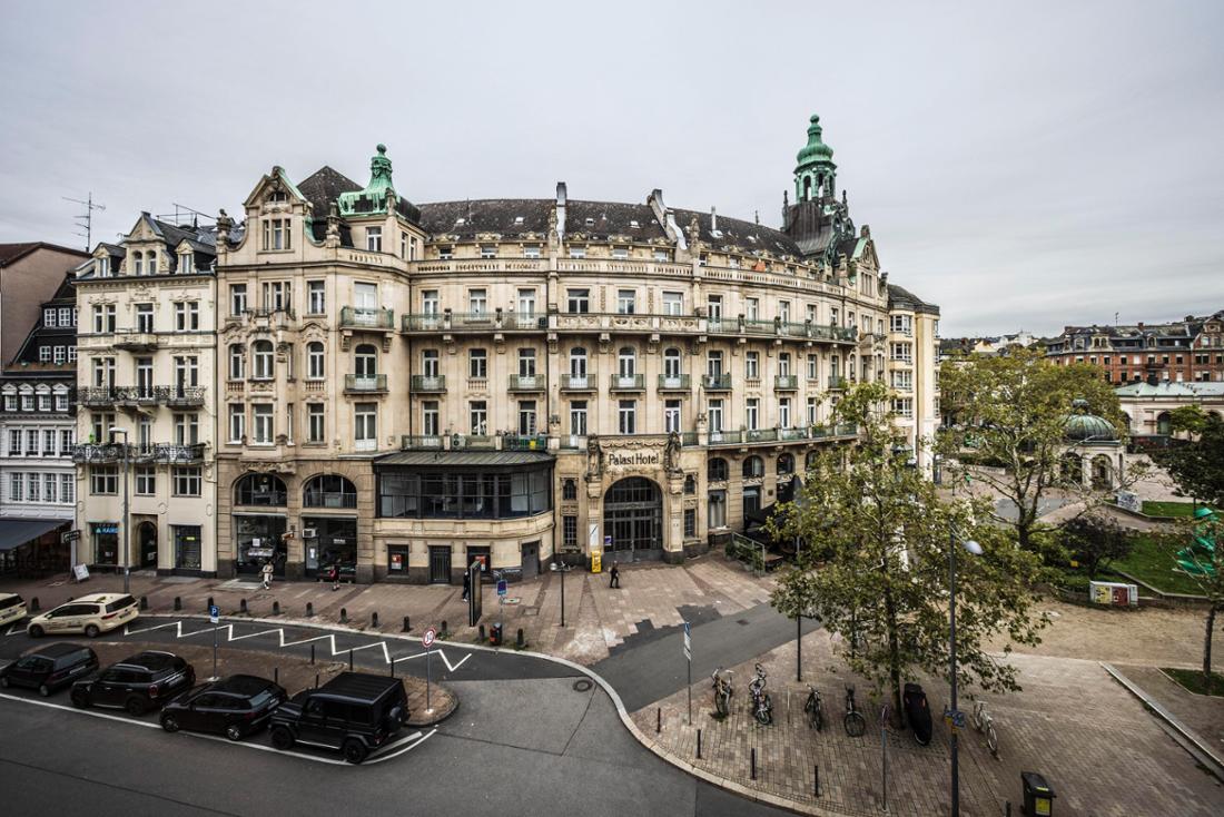 Das denkmalgeschützte Gebäudeensemble des Palasthotels, aufgenommen von der gegenüberliegenden Straßenseite. Die Fassade des neobarocken Hauses ist markant.