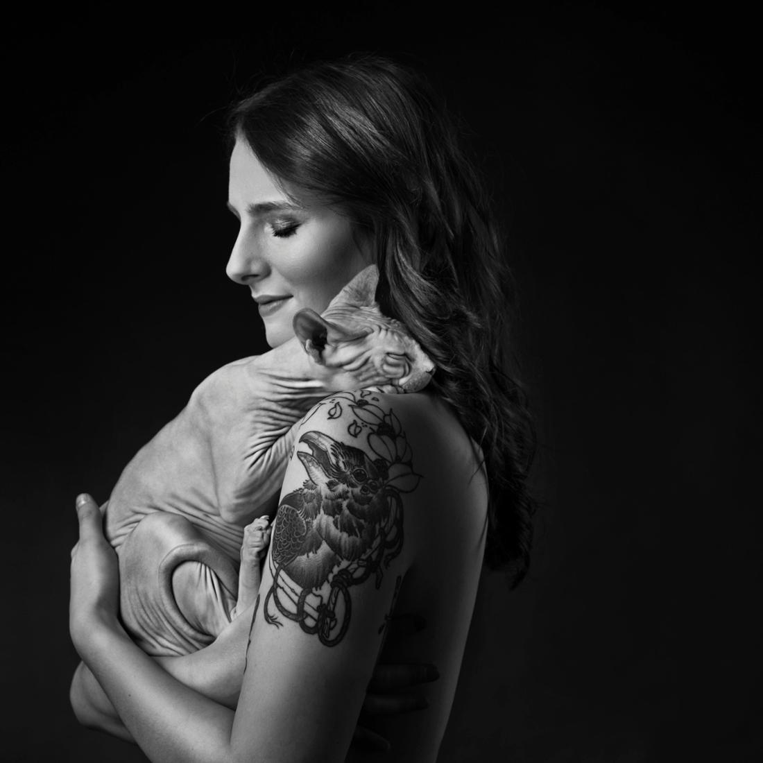 Eine Frau mit Tattoo umarmt ihre Nackkatze