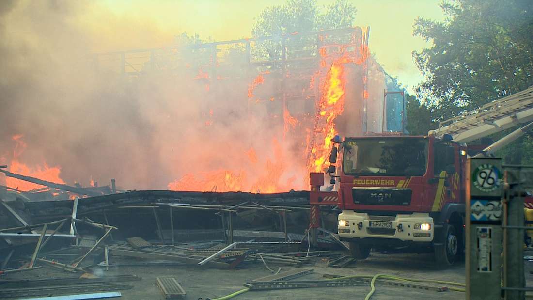 Ein brennendes Gebäude, davor steht ein Feuerwehr-Fahrzeug.
