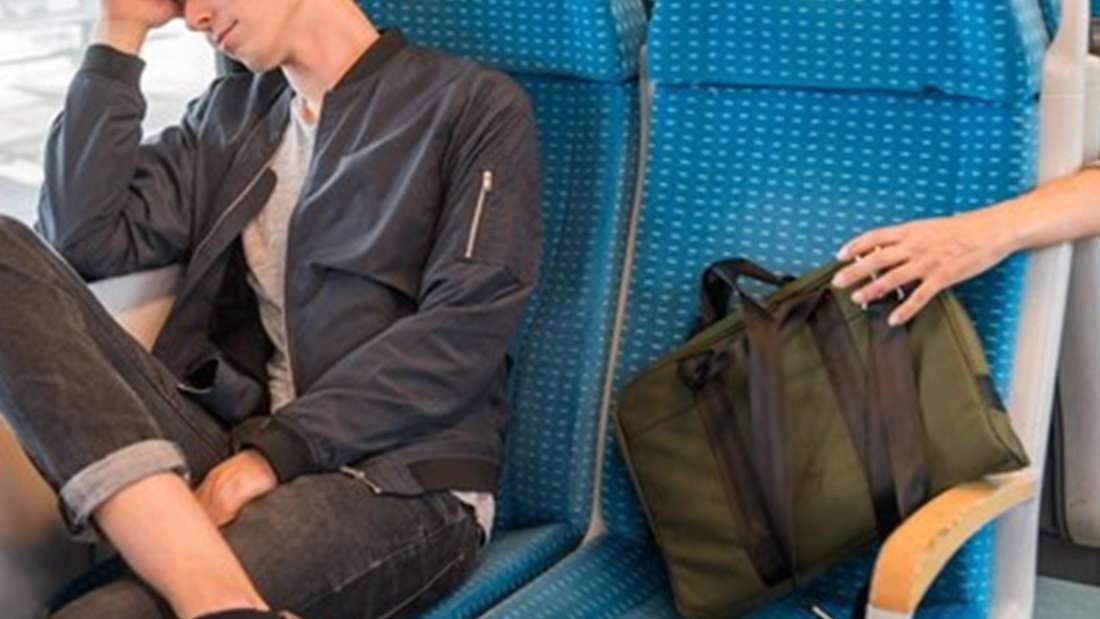 Ein Reisender schläft in einem Zug. Ein Unbekannter greift nach seinem Rucksack. 