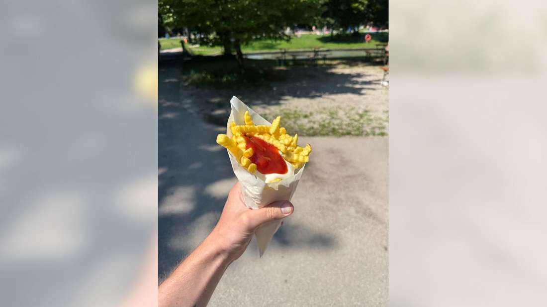 Eine Hand hält eine Portion Pommes. 