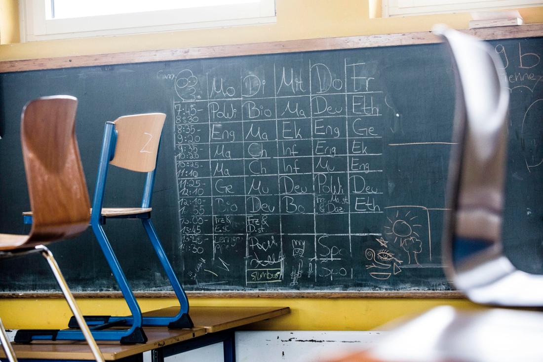 Symbolfoto: Blick in einen Klassenraum. Die Stühle sind hochgestellt. An der Tafel steht ein Stundenplan angeschrieben. 
