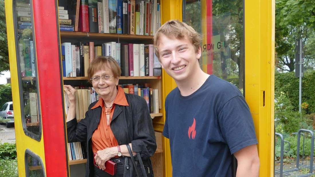Treffpunkt für Bücherfreunde: Die umgebaute Telefonzelle vor dem Rathaus in Karlsfeld begeistert Jung und Alt. Jugendratsvorsitzender Lorenz Stabl und die  ehrenamtliche Helferin Doris Kaps freuen sich über die große Resonanz.