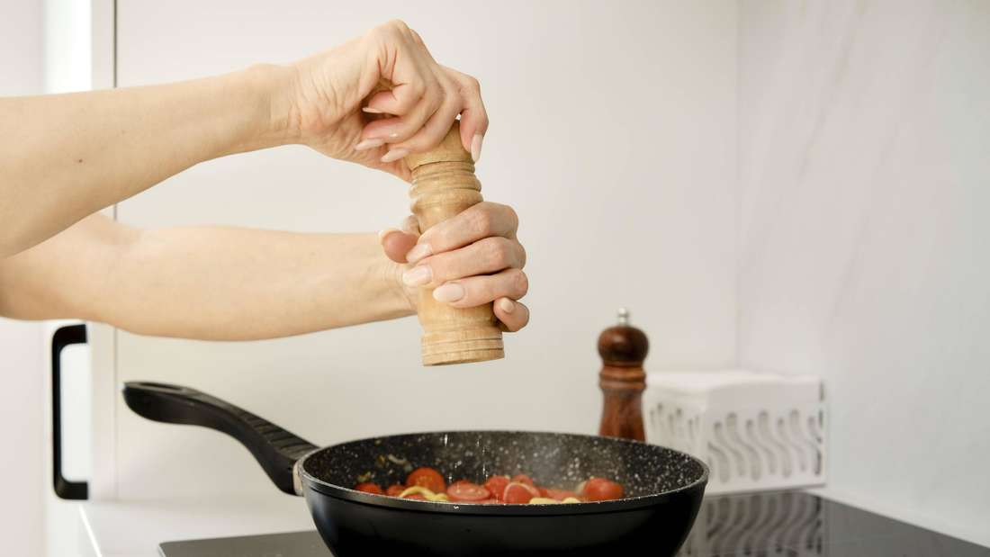 Eine Hand mahlt Salz über einer Pfanne.