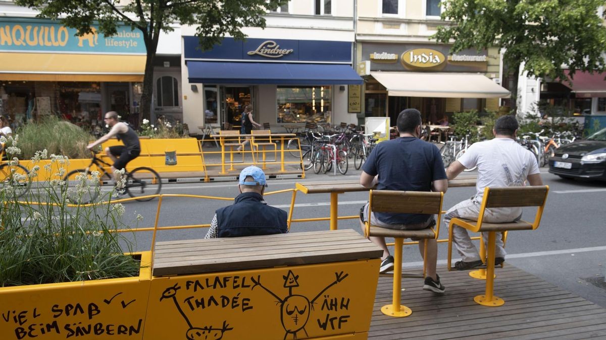 Passanten sitzen in einem Parklet an der Bergmannstraße in Kreuzberg.