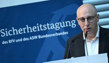 Sinan Selen, Vizepräsident des Bundesamtes für Verfassungsschutz spricht bei einer Sicherheitstagung. Er steht vor einem Mikrofon. Im Hintergrund sieht man ein blaues Plakat mit dem Titel der Veranstaltung.