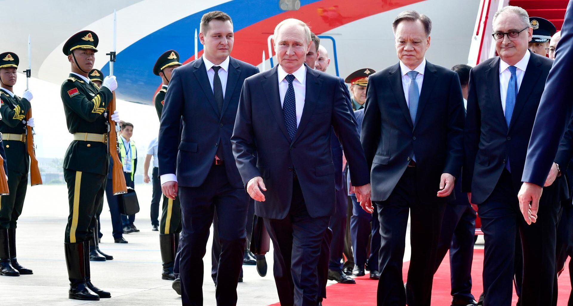 Russands Präsident Putin schreitet über einen roten Teppich. Links und rechts neben ihm stehen weitere Männer in Anzügen. Im Hintergrund sieht man Soldaten, die salutieren.