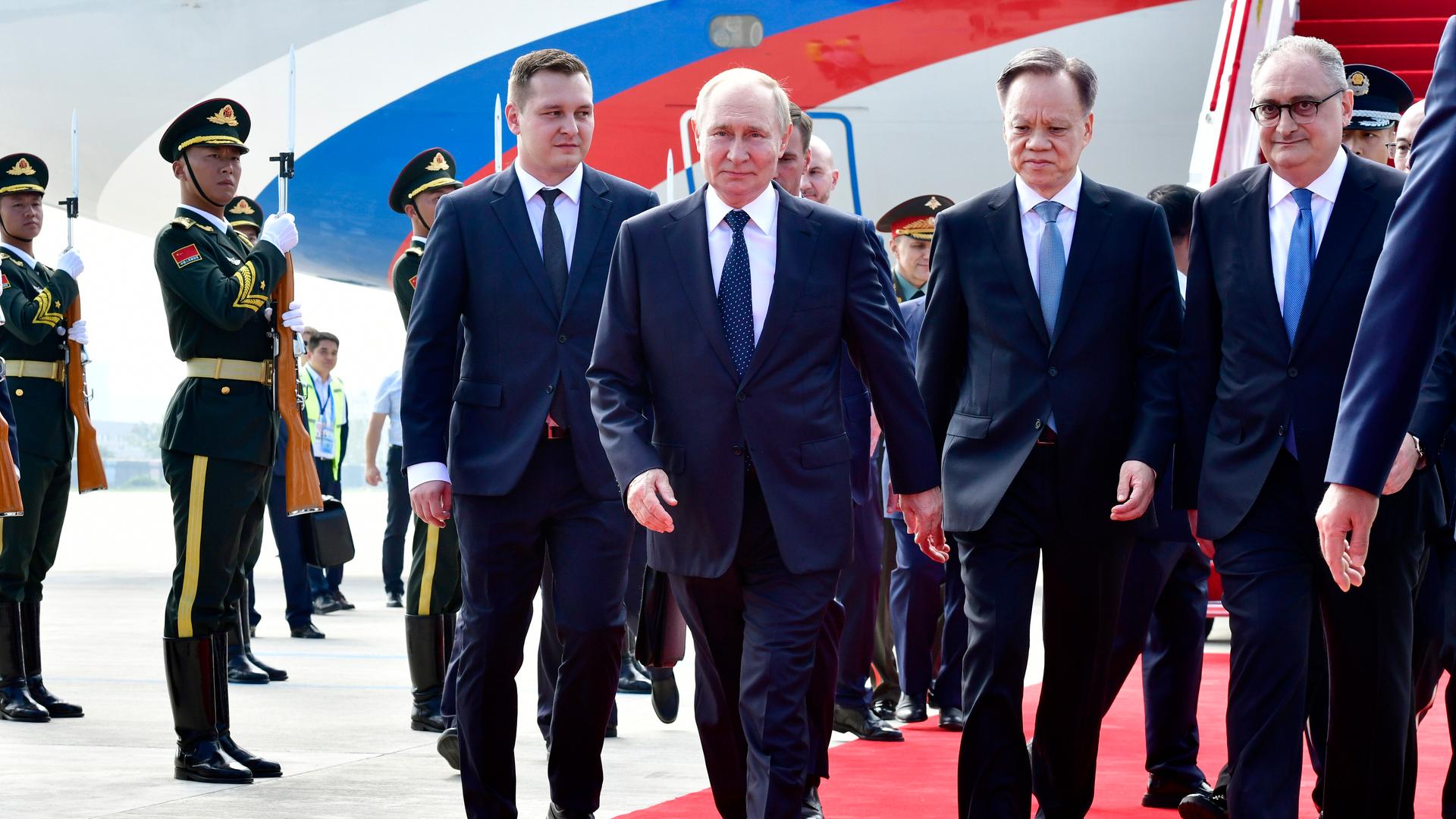 Russands Präsident Putin schreitet über einen roten Teppich. Links und rechts neben ihm stehen weitere Männer in Anzügen. Im Hintergrund sieht man Soldaten, die salutieren.