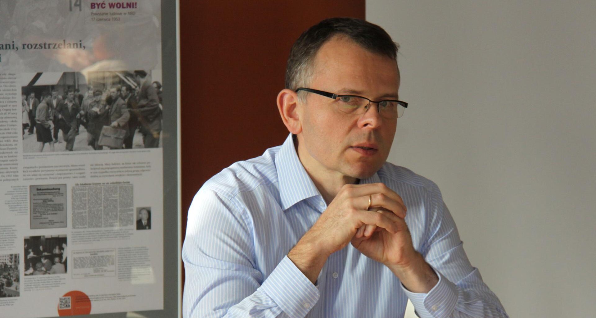 Krzysztof Ruchniewicz sitzt mit gefalteten Händen an einem Schreibtisch.