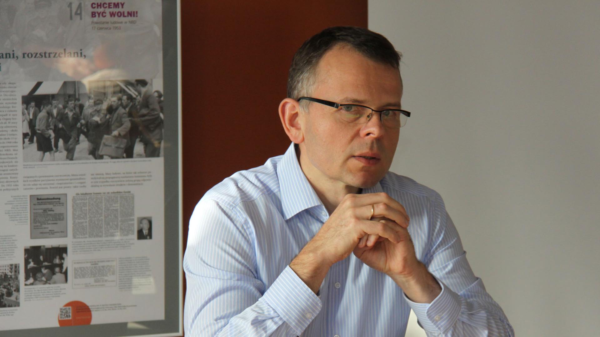 Krzysztof Ruchniewicz sitzt mit gefalteten Händen an einem Schreibtisch.