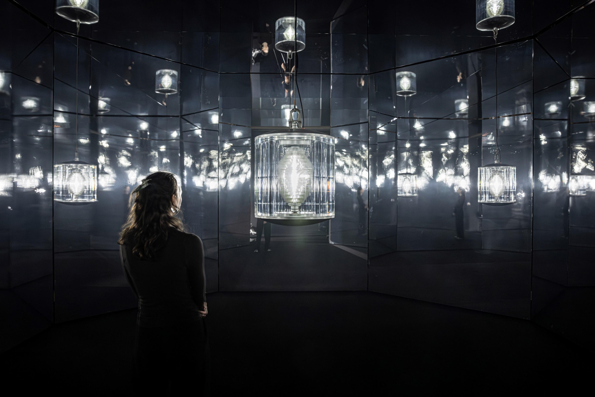 Person betrachtet eine Reihe von leuchtenden Lichtern in einem reflektierenden, spiegelartigen Raum mit futuristischer Atmosphäre.