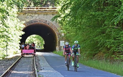 Ein Radweg entlang einer Bahntrasse mit einer Draisine darauf.