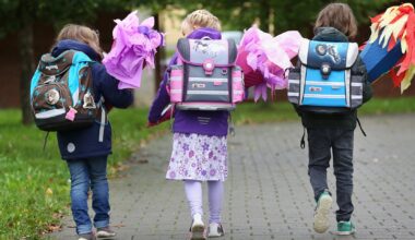 Drei Schulkinder laufen mit Rucksack und Schultüte nebeneinander,