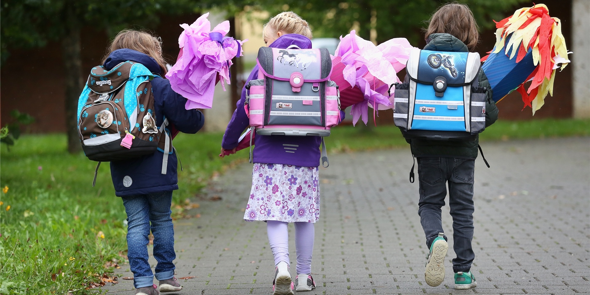 Drei Schulkinder laufen mit Rucksack und Schultüte nebeneinander,